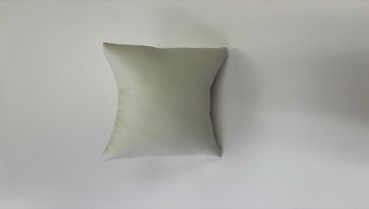 A pillow that is on the ground in front of a wall.